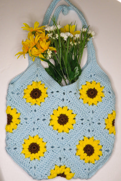 Crocheted bag with sunflower pattern holding flowers on a white background
