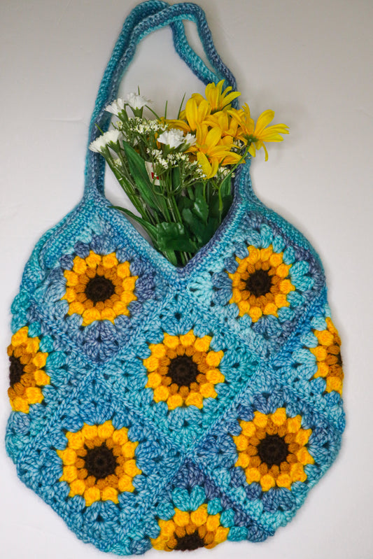 Crocheted bag with sunflower pattern holding flowers on a white background