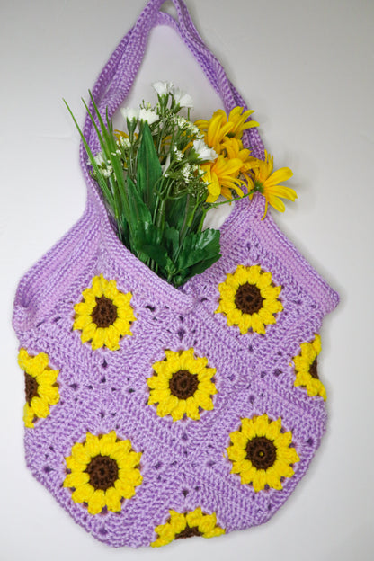 Purple crochet bag with yellow sunflower patterns filled with flowers on a white background