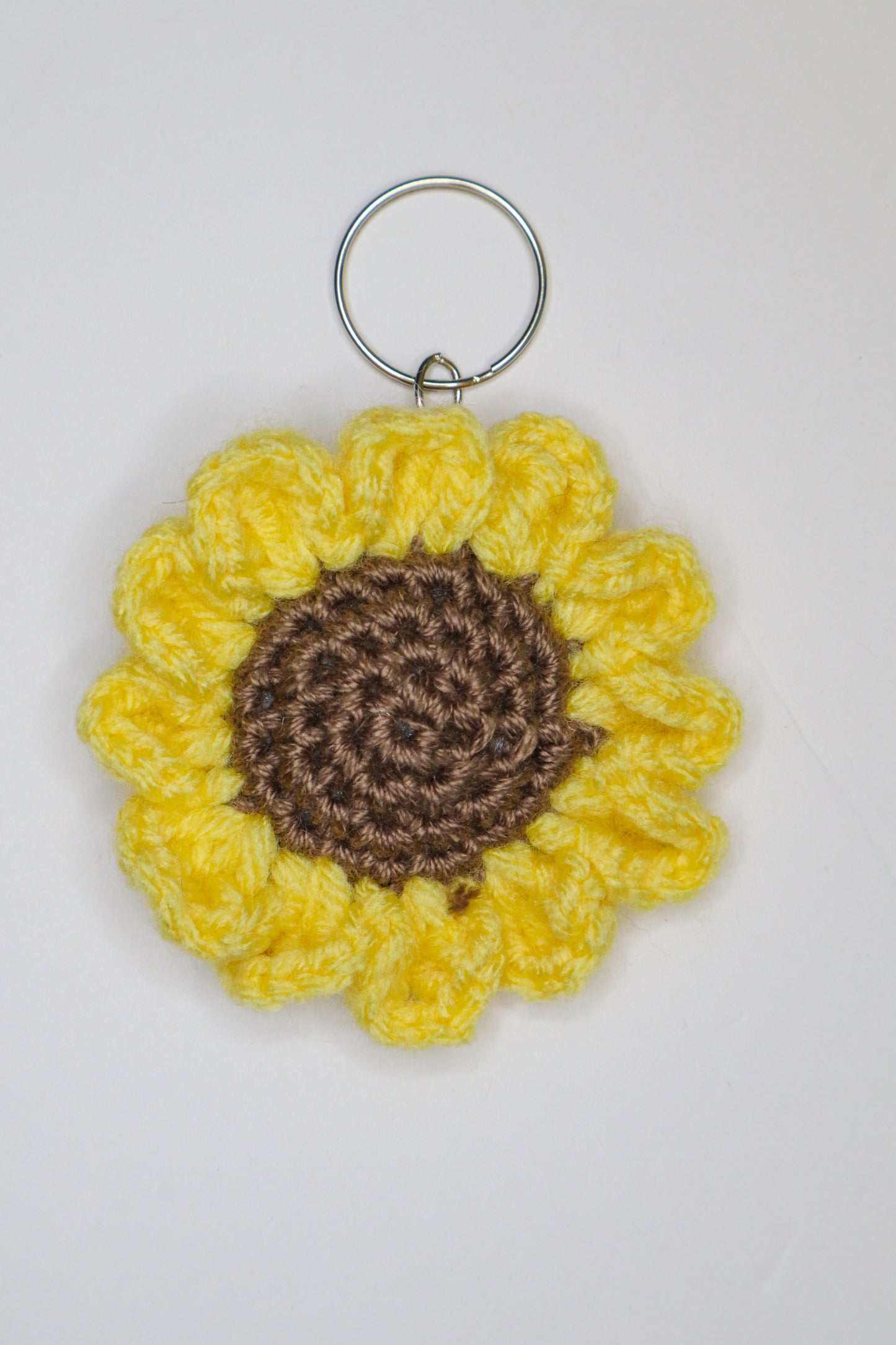 Crocheted sunflower keychain with yellow petals and brown center on a white background