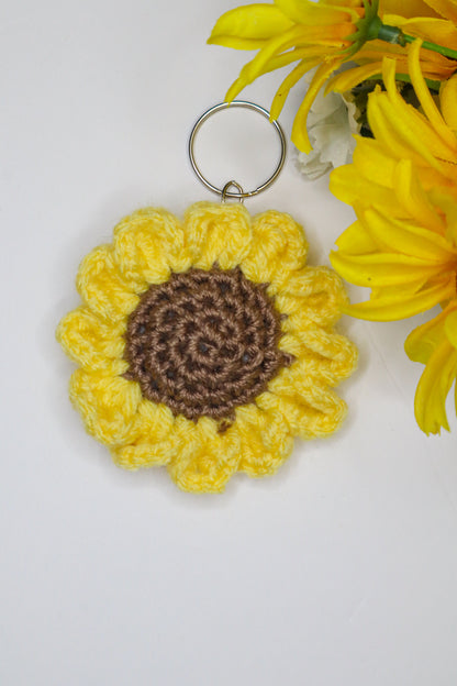 Crocheted sunflower keychain with brown center on a white background with yellow flowers.