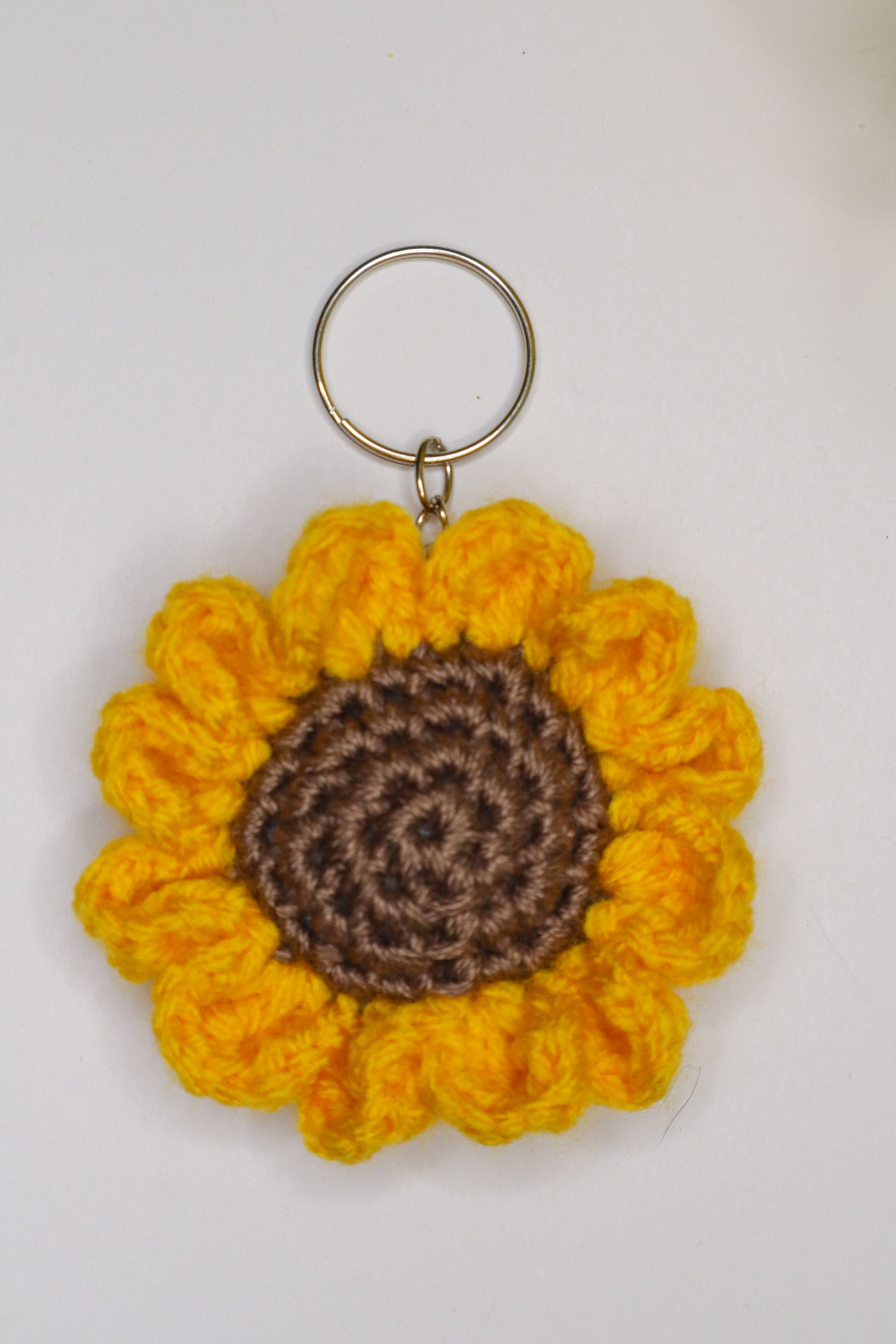 Crocheted sunflower keychain with yellow petals and brown center on a white background