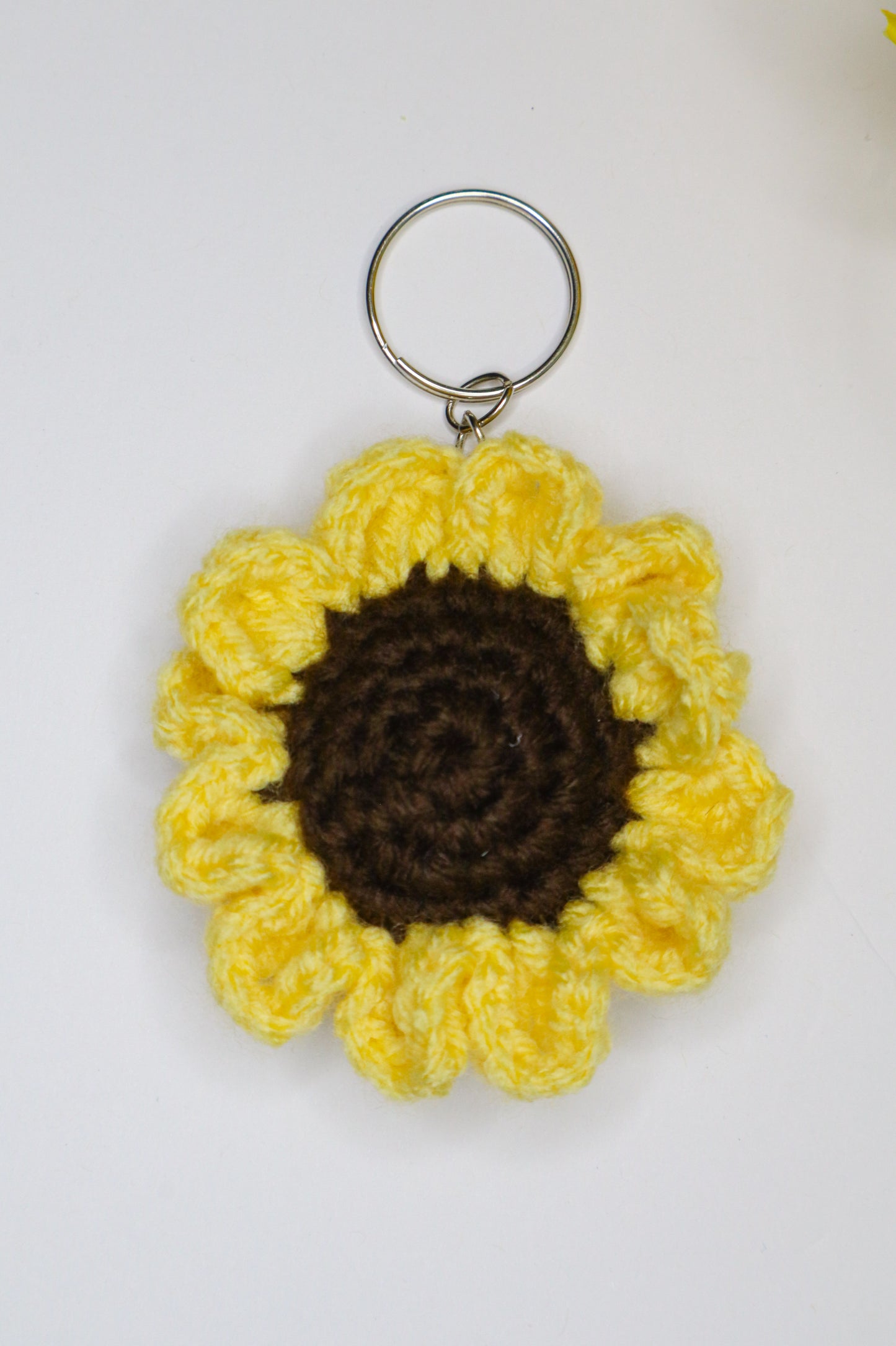 Crocheted sunflower keychain with yellow petals and brown center on a white background