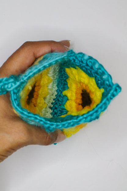 Hand holding a crocheted square with sunflower pattern against a white background